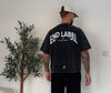 Person wearing a black 'END LABEL' t-shirt standing in a room with a plant.